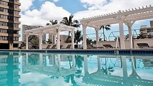 A swimming pool with white pergolas and lounge chairs, surrounded by palm trees and buildings. - Beautiful OCEAN & CANAL View - Renovated - Waikiki Studio (Honolulu)