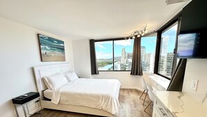 A hotel room with a bed, a desk, a TV, and a large window with a city view. - Beautiful OCEAN & CANAL View - Renovated - Waikiki Studio (Honolulu)