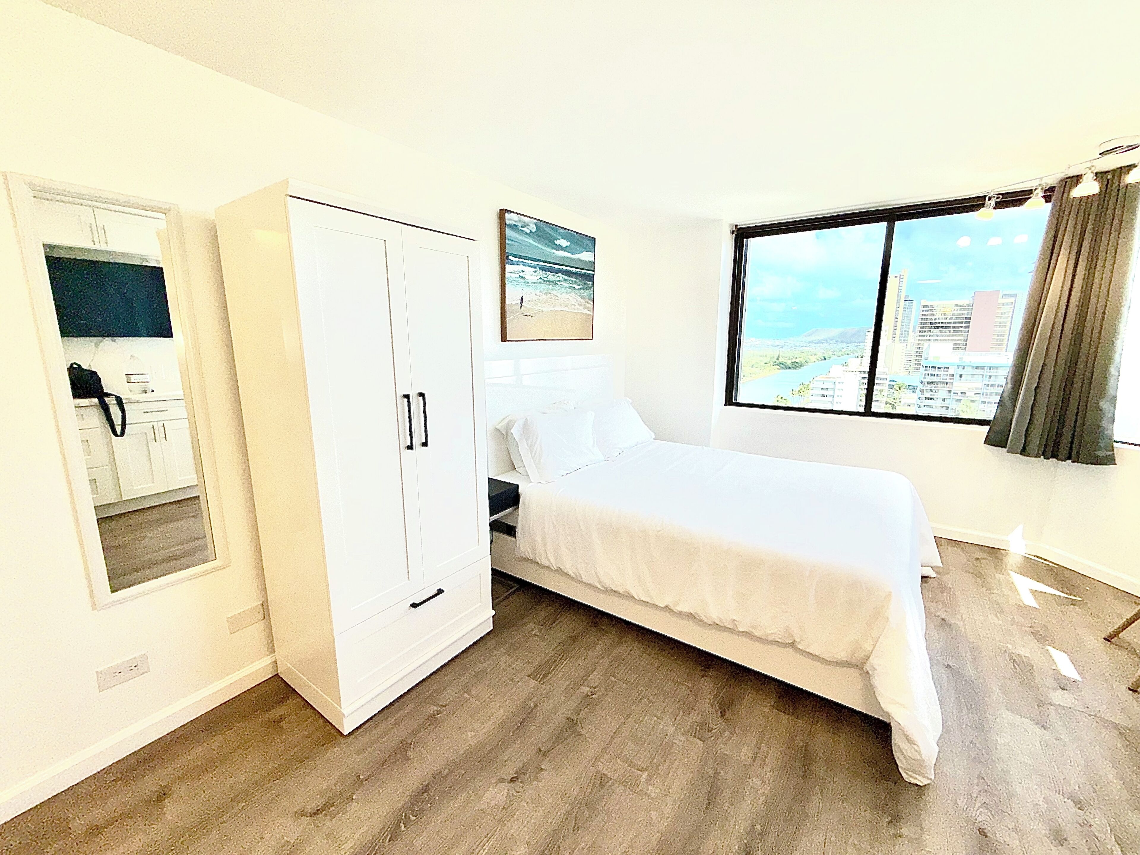 Una camera da letto con un letto, un armadio, una finestra vista città e un quadro appeso al muro.