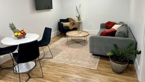 A modern living room with a round coffee table, a grey sofa, a black armchair, and a dining table with fruit.