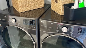 Two front-loading washing machines with control panels, baskets containing laundry supplies, and a spray bottle on top.