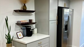 A modern kitchen with grey cabinetry, a stainless steel refrigerator, and a small round table with a potted plant.