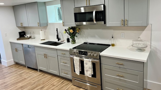 A modern kitchen with grey cabinets, stainless steel appliances, and a wooden floor.