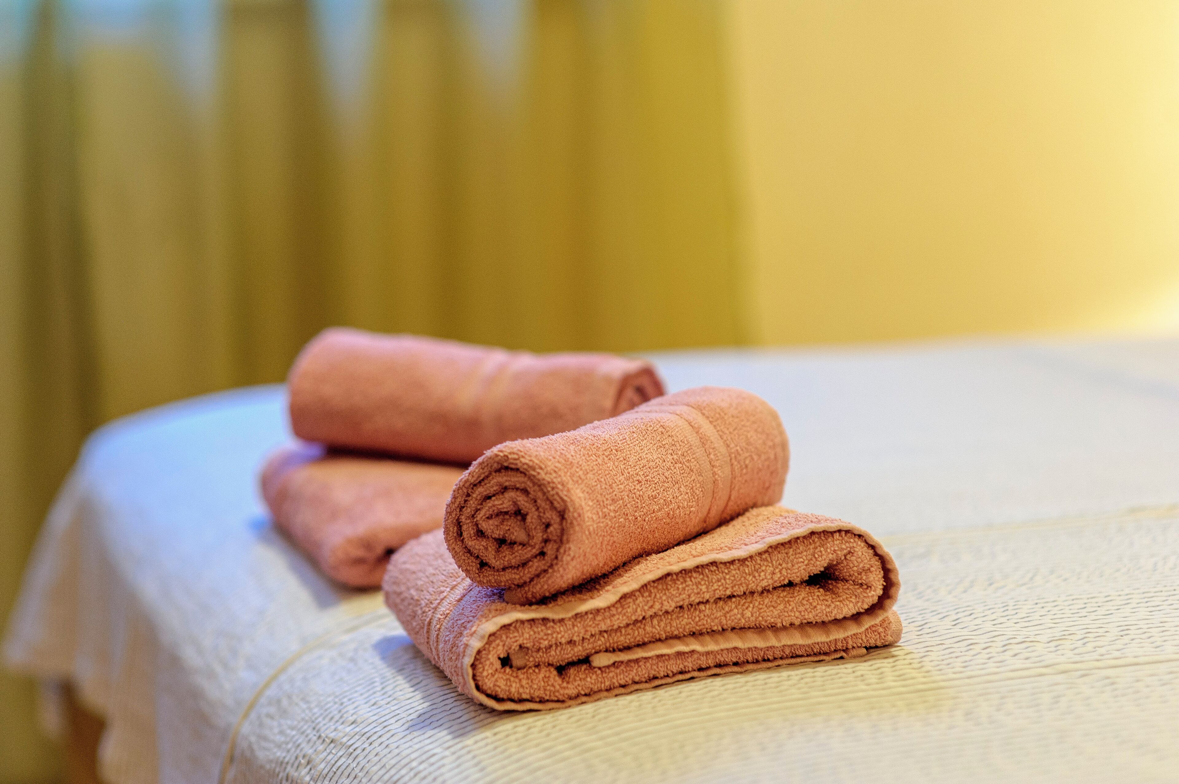 A neatly folded brown towel on a bed with a textured white cover.