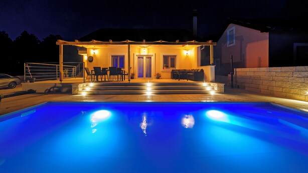 Una piscina con un área de patio techada, un muro de ladrillo y un edificio con puerta y ventanas.