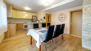 Un comedor con una mesa dispuesta para cuatro, una cocina al fondo y un reloj en la pared.