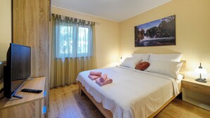 Un dormitorio con cama, televisión, mesita de noche, lámpara y un cuadro en la pared.