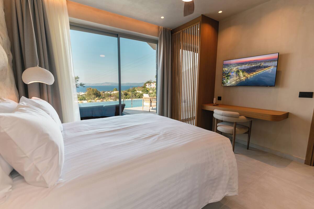 Une chambre d’hôtel avec un grand lit, un bureau, une télévision et une vue sur la mer.