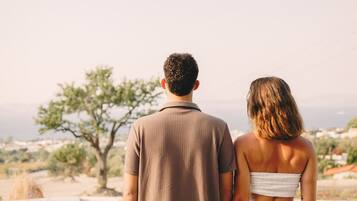 Un couple se tient près d’une piscine, avec vue sur un arbre et des bâtiments situés au loin.