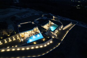 Ett modernt semesterhotell med två pooler, utomhusområde med sittplatser och en väl upplyst gångväg.