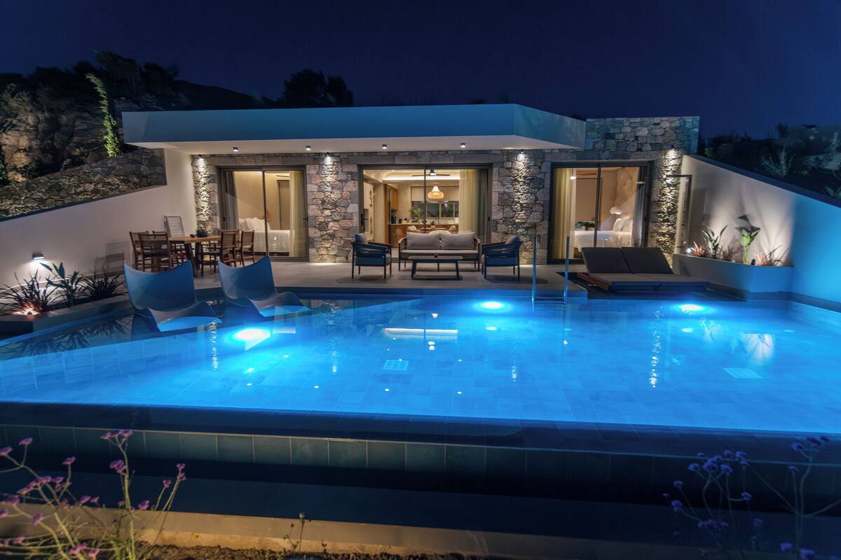 Une maison moderne dotée d’une piscine, d’un espace salon extérieur et d’une façade en pierre.