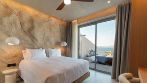A modern bedroom with a large bed, a ceiling fan, and a view of the outdoors through a sliding glass door.