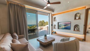 A modern living room with a large flat-screen TV, a ceiling fan, and a view of the outdoors.