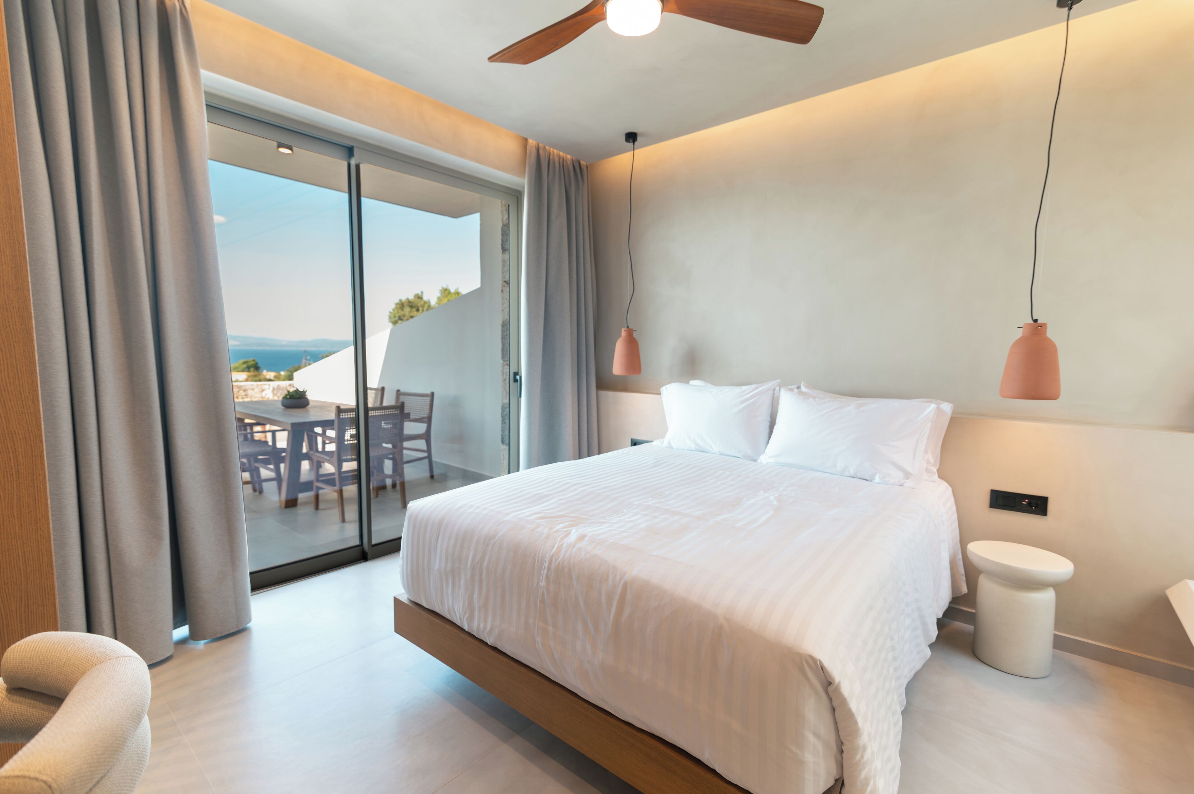 Une chambre moderne avec un grand lit, un ventilateur de plafond et une vue sur l’extérieur grâce à une porte-fenêtre coulissante.