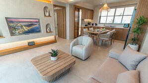 A modern living room with a flat-screen TV, a wooden coffee table, a beige sofa, and a dining area with a table and chairs.