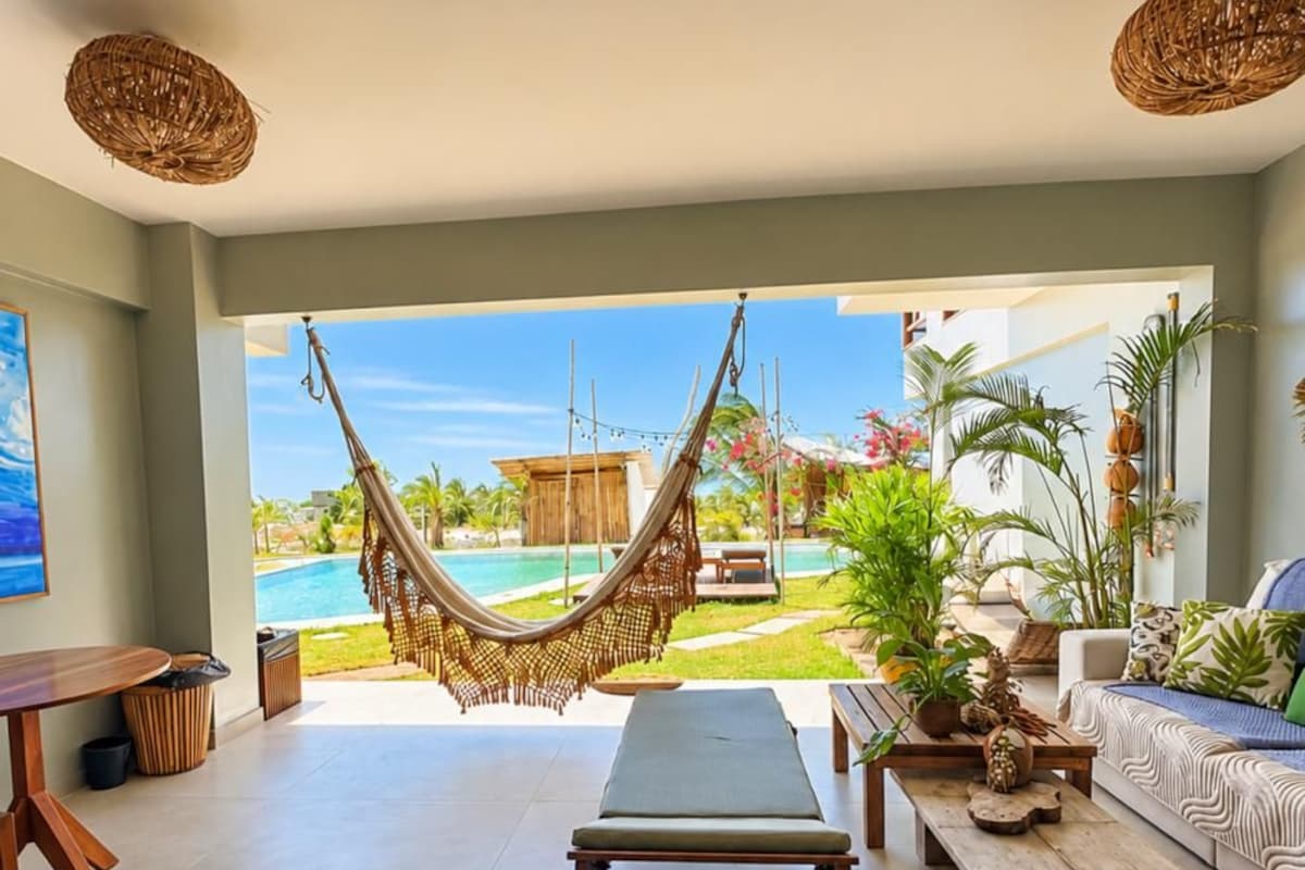 Una habitación con una hamaca, un sofá, una mesa de madera y vista a una piscina.