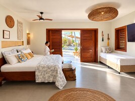 Habitación de hotel con cama, reposabajares y ventilador de techo, con vista a la playa.