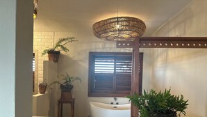 Un baño con una bañera independiente, una ventana con persianas y plantas en macetas.