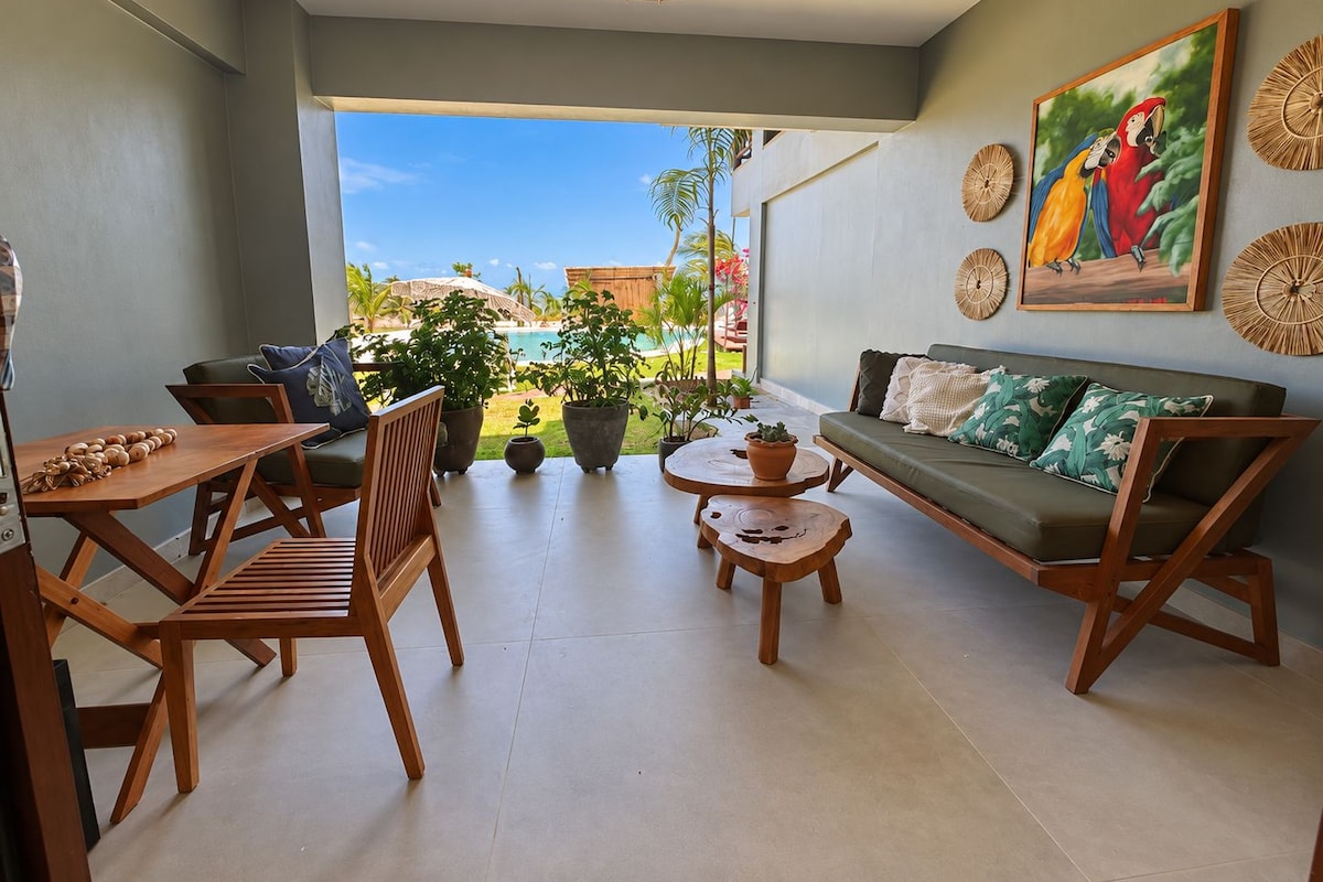 Una sala moderna con sofá, sillas, mesa de centro y mesa de comedor. Hay un ventanal con vistas a una piscina y vegetación.