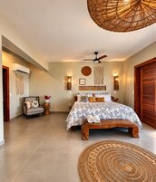 Un dormitorio con cama, ventilador de techo, alfombra tejida y aire acondicionado de pared.