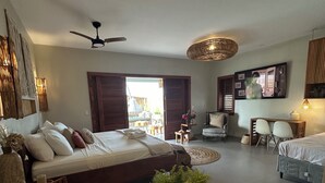 Amplia sala de estar con una cama grande, una mesa de comedor con un florero, un ventilador de techo y vistas al exterior.