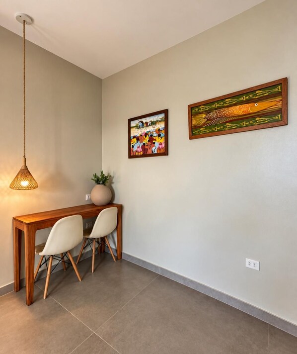 Un área de comedor con una mesa y sillas de madera, una lámpara colgante y dos obras de arte enmarcadas en la pared.