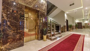 Un hall d’hôtel avec un sol en marbre, une moquette rouge, un escalier et un comptoir d’accueil.