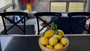 A modern kitchen with a marble backsplash, a wooden bowl of lemons on the counter, and a view of greenery outside.