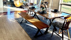 A modern dining area with a wooden table, benches, and chairs. There are large windows offering a view of the outdoors.