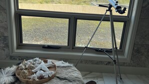 A telescope on a tripod by a window overlooking a coastal landscape.
