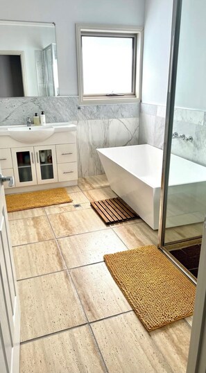 A modern bathroom with a marble vanity, a large window, a bathtub, and two textured mats on the floor. - Off the grid accommodation in a Beautiful slice of Paradise
(Wye)