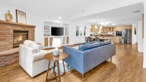 Ein geräumiges Wohnzimmer mit Kamin, einer Couch, einem Fernseher und einer Küche im Hintergrund.