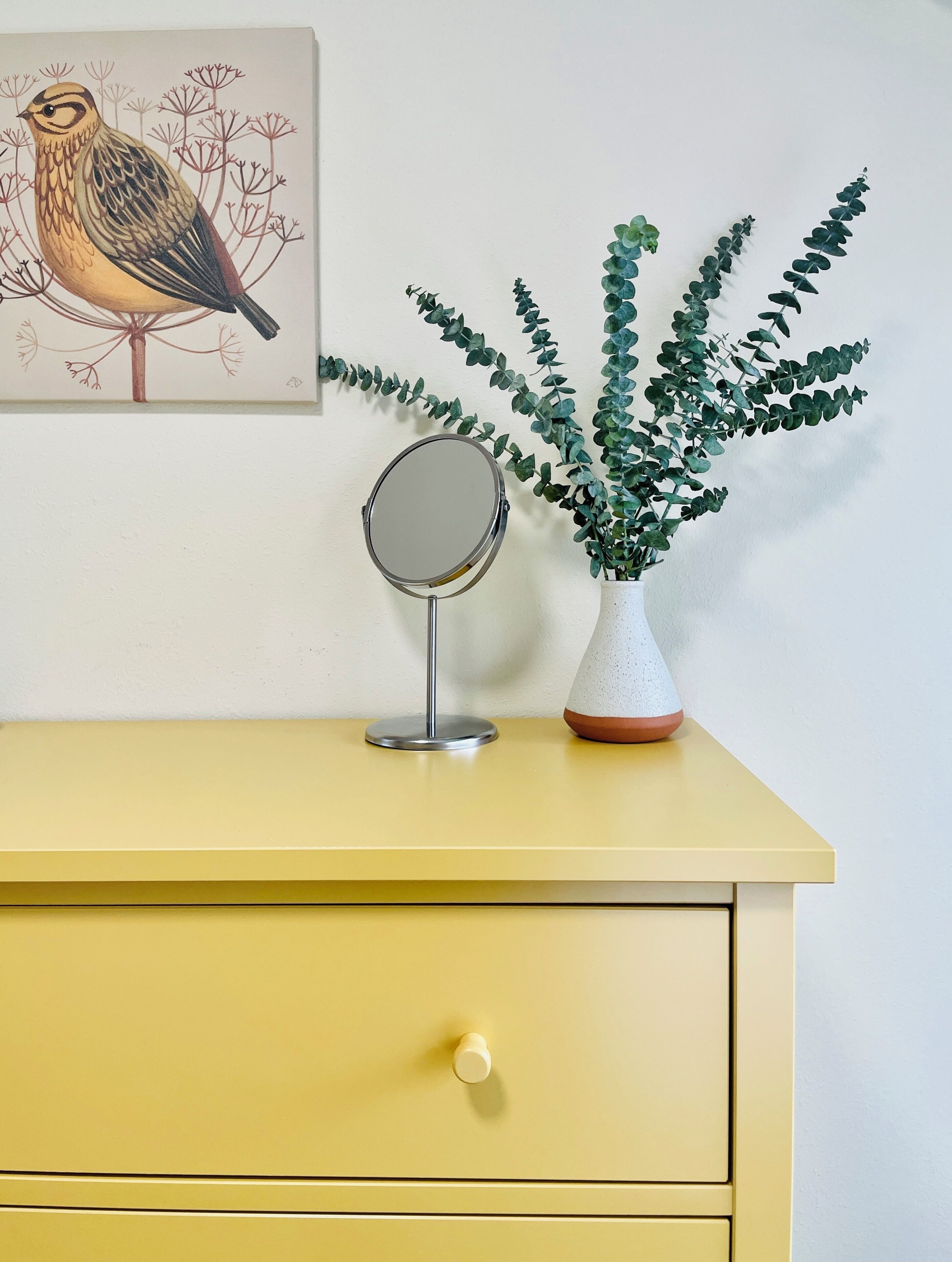 A yellow dresser with a round mirror and a plant in a white pot.