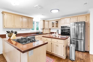 Une cuisine avec des meubles de rangement en bois, un réfrigérateur en acier inoxydable, une cuisinière à gaz et une poubelle.