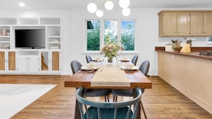 Ein zeitgemäßer Essbereich mit Holztisch, Stühlen und einem Fernseher im Hintergrund.