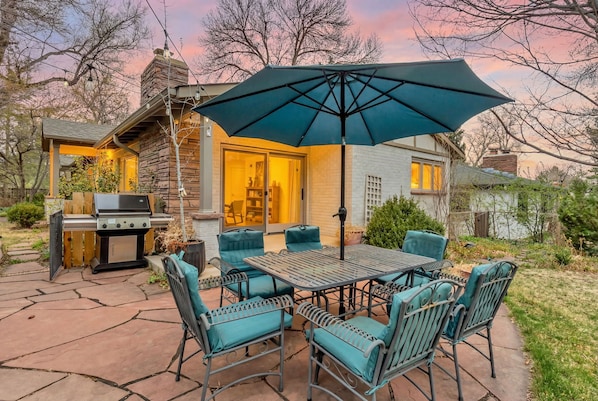 Une terrasse extérieure équipée d’un barbecue, d’une table à manger, de chaises et d’un parasol.