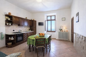 A kitchen with wooden cabinets, a dining table with chairs, a window with curtains, and a radiator. - I Castagnini
Your Corner of Tuscany: relaxation and discovery (MONTECATINI VAL DI CECINA)