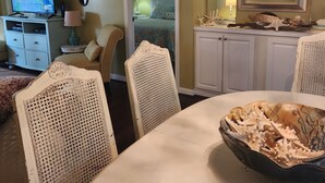 A dining area with a round table, chairs, and a decorative bowl. A television is on a stand in the background. - Quiet 3rd floor King condo Pawleys Island Golf Course WiFi, SC State Park Pass (Pawleys Island)