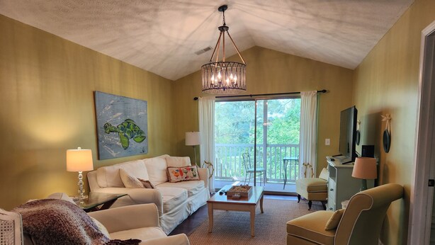 A cozy living room with a sofa, armchair, and a coffee table. There is a painting on the wall, a lamp, and a television on a stand. - Quiet 3rd floor King condo Pawleys Island Golf Course WiFi, SC State Park Pass (Pawleys Island)