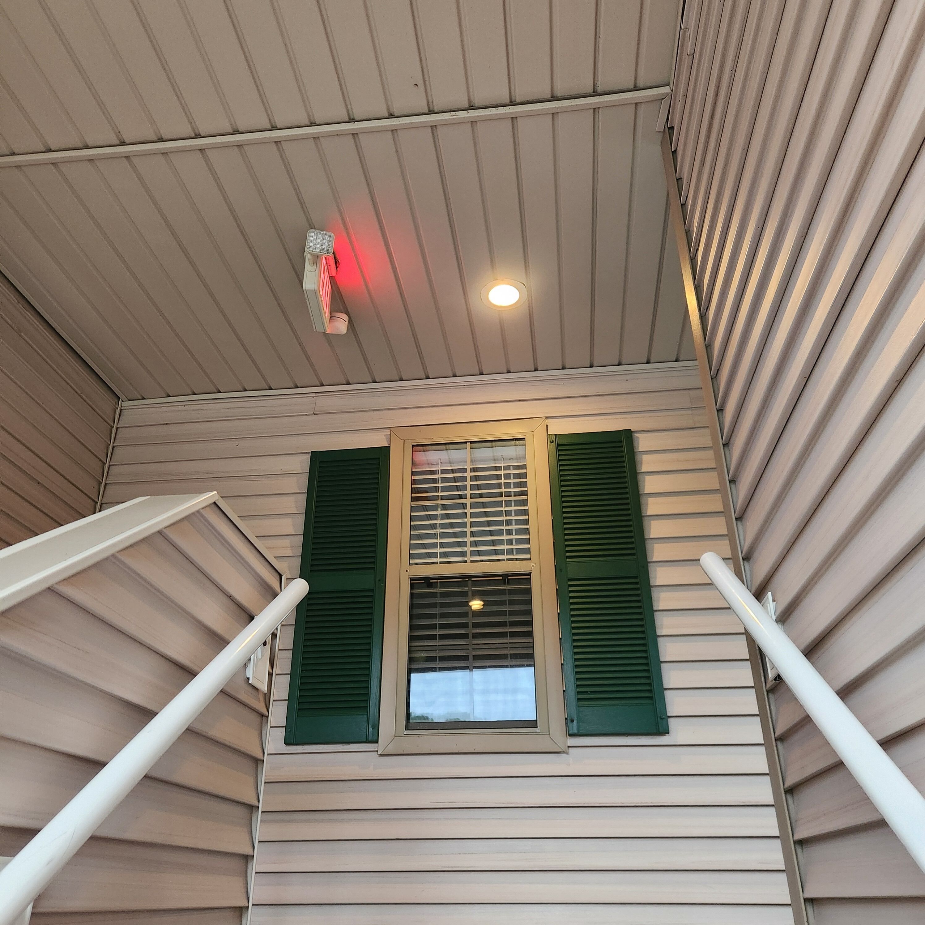 A room with a sloped ceiling, a window with green shutters, and a visible light fixture.