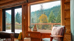 A cozy cabin interior with a large window offering a view of a forested mountain. - Douglas Fir Retreat | Mtn Views + Expansive Deck (Sunshine Valley)