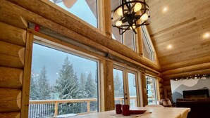 A wooden cabin interior with a large dining table, white chairs, and a ceiling fan. - Douglas Fir Retreat | Mtn Views + Expansive Deck (Sunshine Valley)