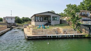 A house with a dock extending into a canal, surrounded by greenery and other buildings. - City Escape - Lakefront + Dock + Firepit + Fishing (Kingsland)