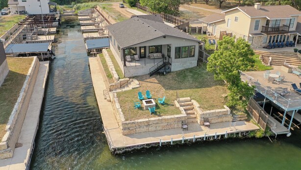 A house with a dock extending into a body of water, surrounded by a grassy yard and a few trees. - City Escape - Lakefront + Dock + Firepit + Fishing (Kingsland)