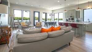 A modern living room with a grey sofa, orange cushions, and a dining area with a round table and chairs. - City Escape - Lakefront + Dock + Firepit + Fishing (Kingsland)