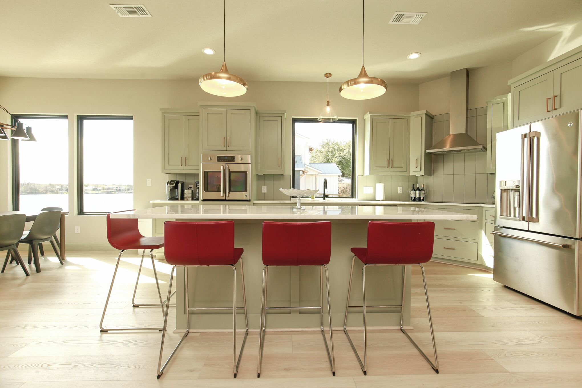 A modern kitchen with a large island, stainless steel appliances, and red bar stools.