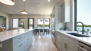 A modern kitchen with a large island, a dining area with chairs, and a view of the outdoors. - City Escape - Lakefront + Dock + Firepit + Fishing (Kingsland)