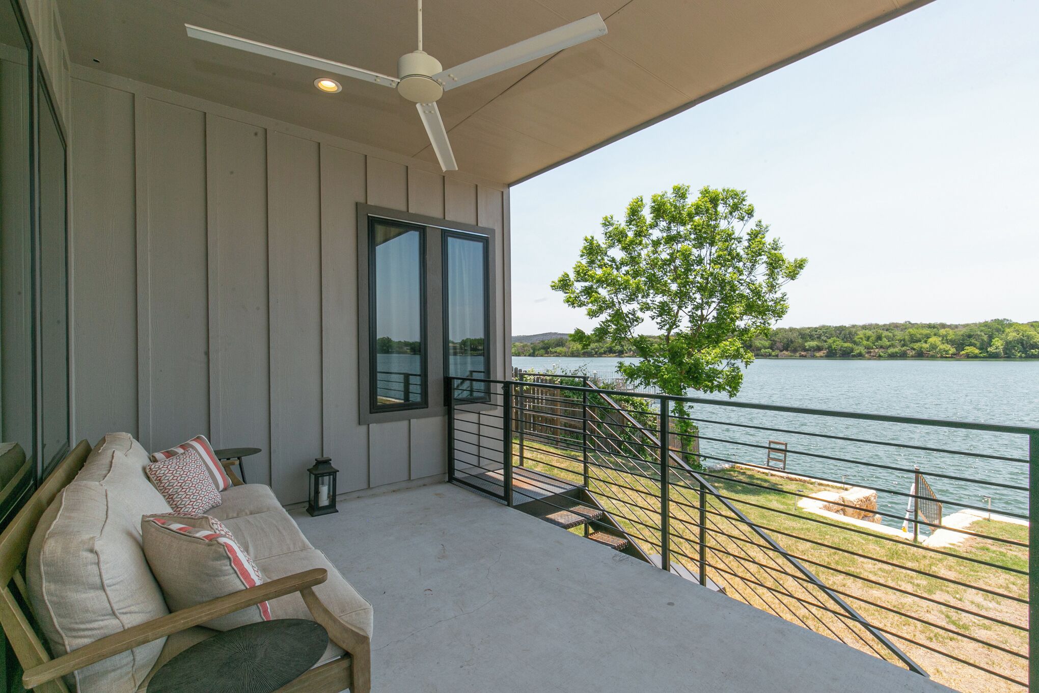 Un balcone con vista su un lago, un divano con cuscini, una ventola a soffitto e una lanterna.