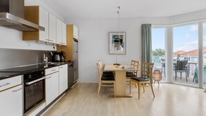 Une cuisine moderne avec des meubles blancs, des appareils en acier inoxydable et une table à manger en bois, accompagnée de chaises.