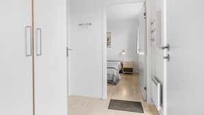 Un couloir menant à une chambre à coucher équipée d’un lit, d’une table de chevet et d’un radiateur.